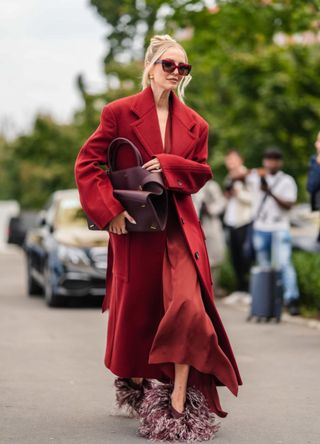 Leonie Hanne wears dark red sunglasses, dark red wool Ferragamo coat, dark red marron Ferragamo leather bag, dark red Ferragamo pants, dark red light pink feathered Ferragamo shoes, outside Ferragamo, during the Milan Fashion Week Spring/Summer 2024-2025 on September 21, 2024 in Milan, Italy