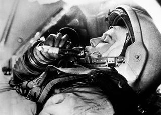 black and white photograph of Valentina Tereshkova in her flight suit eating from a pouch.