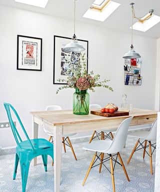 A white dining area with rise and fall pendants over a wooden dining table and blue metal chair