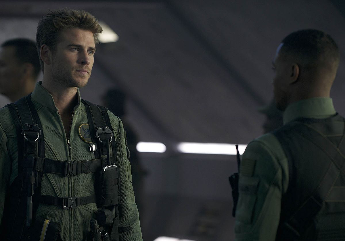 Liam Hemsworth in a flight suit talks to a colleague