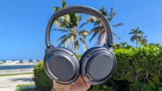 The Treblab Z7 Pro noise-cancelling headphones held aloft against a backdrop of a coastal street with palm trees