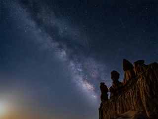 the milky way stretches across the night sky behind a large rock formation.