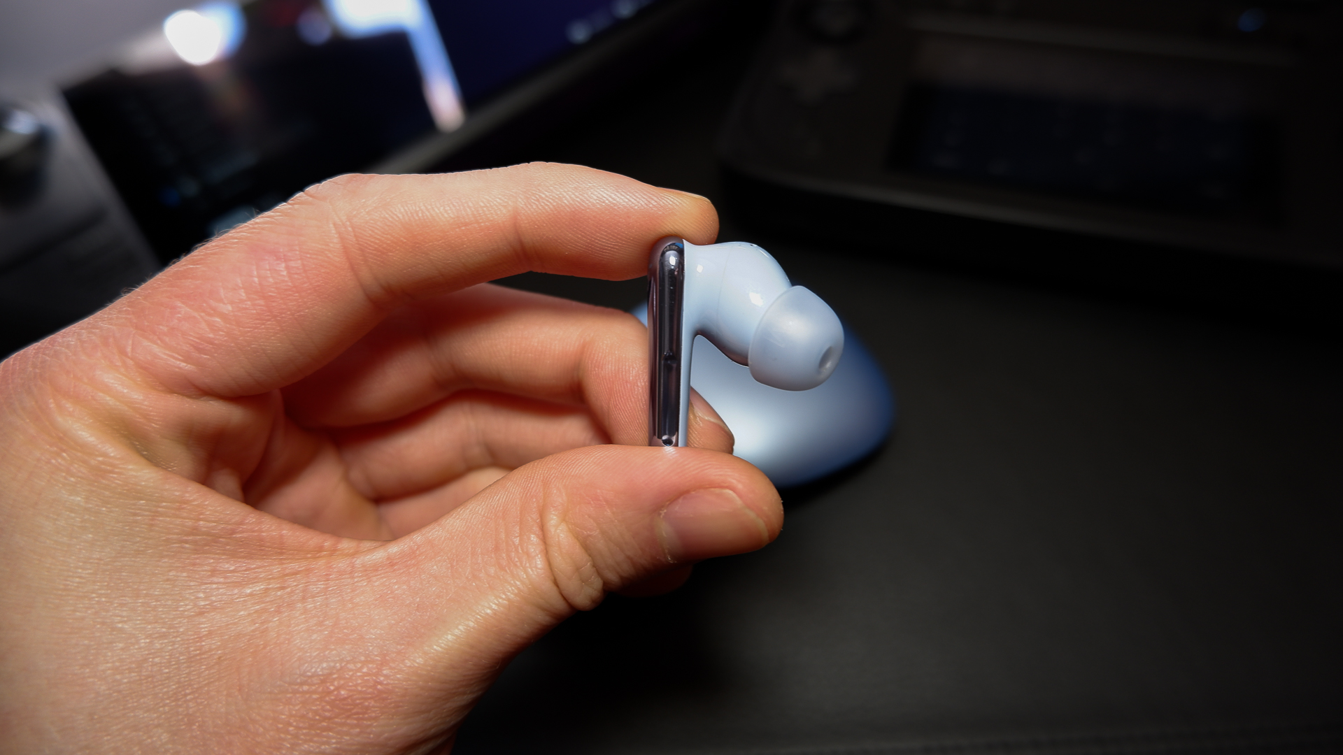 Soundcore Liberty 4 Pro earbuds on a black desk with various handheld gaming PCs.