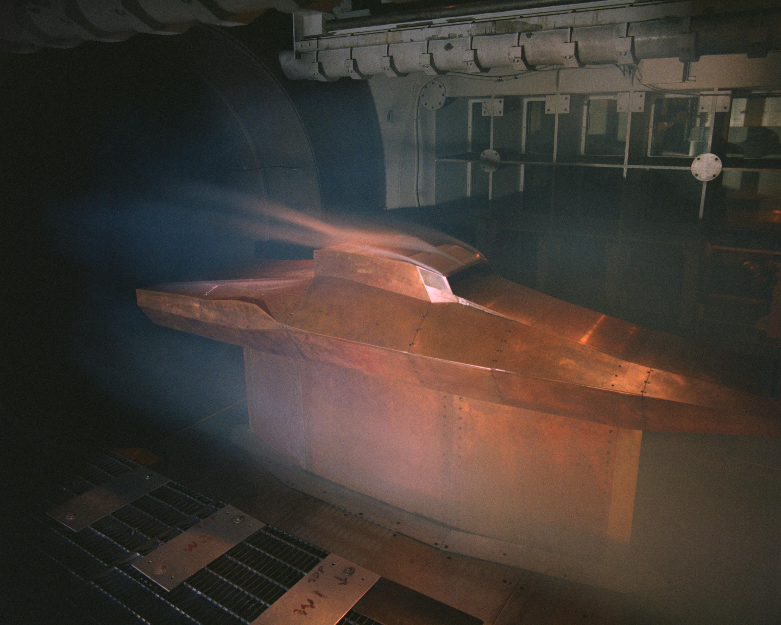 A scale model of a hypersonic flight vehicle lays upside down in a wind tunnel facility.