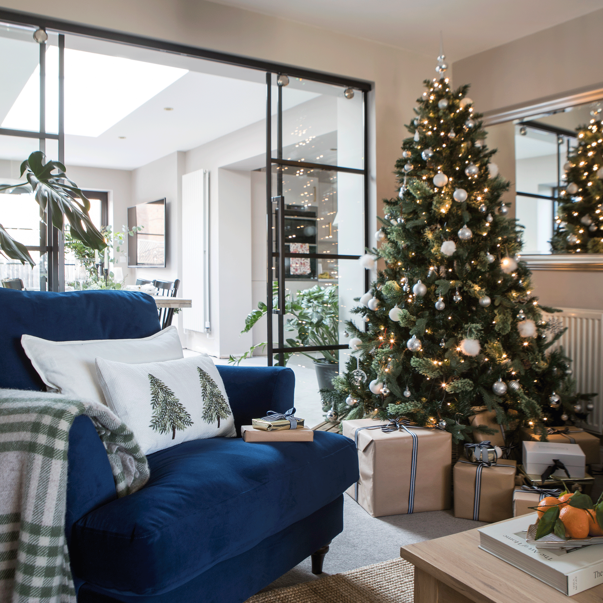 a living area with a blue armchair beside a Christmas tree with glass internal doors leading into a bright dining area