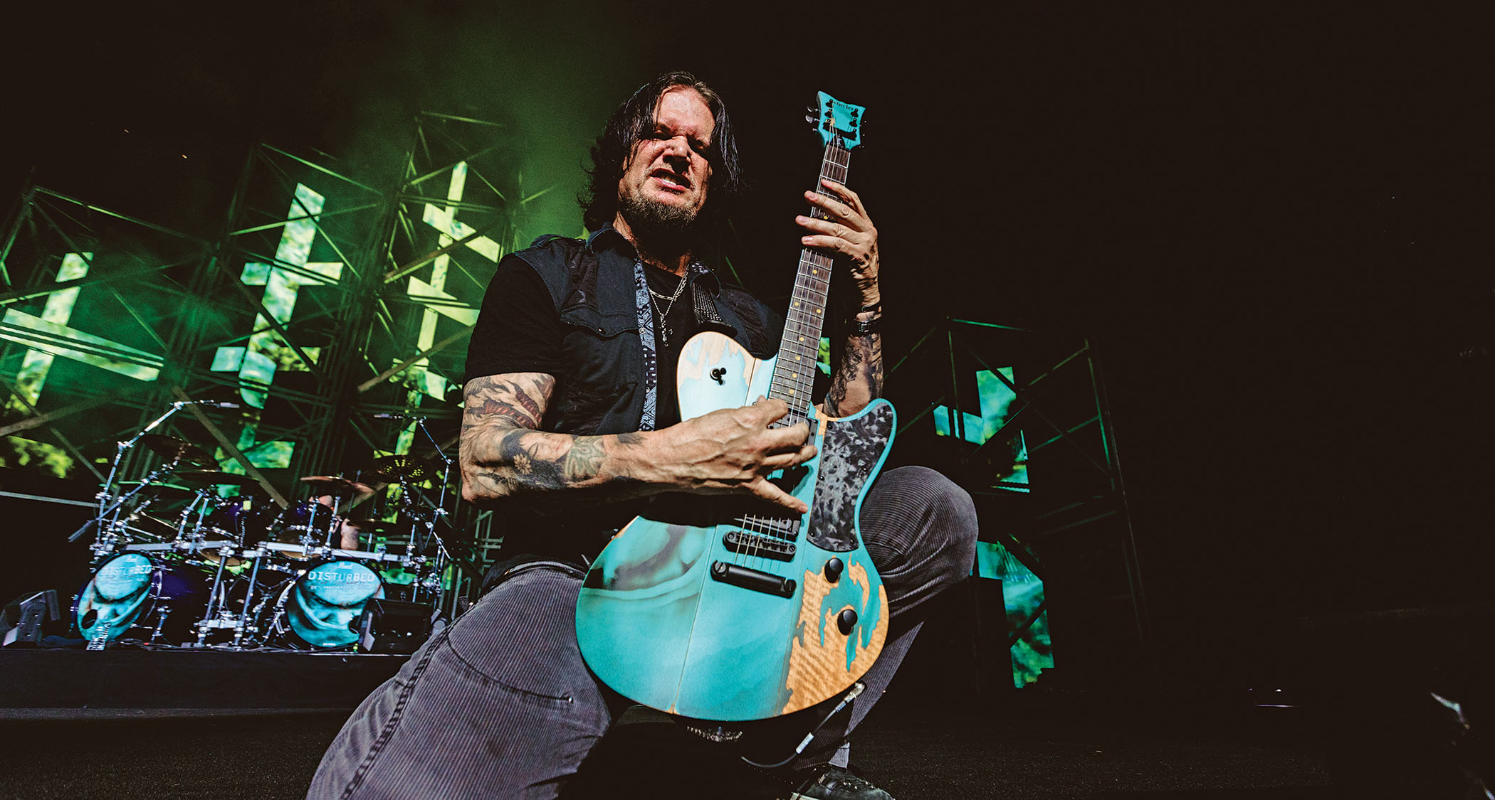 Dan Donegan kneels before the power of the riff with his signature Schecter in Teal, the scars in the finish betraying its status as one of the Disturbed guitarist&#039;s go-to 
