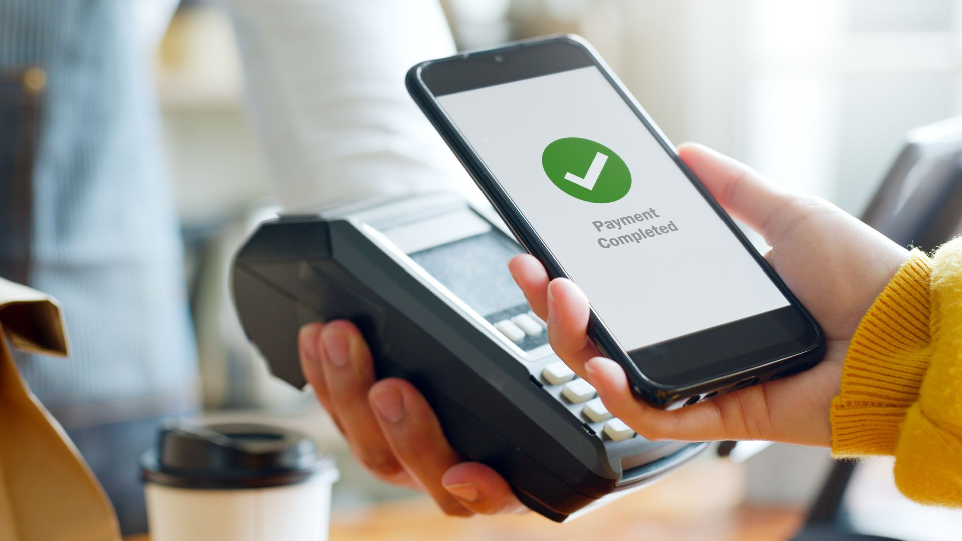 Una mano realizando un pago sin contacto con un teléfono inteligente en un terminal de tienda