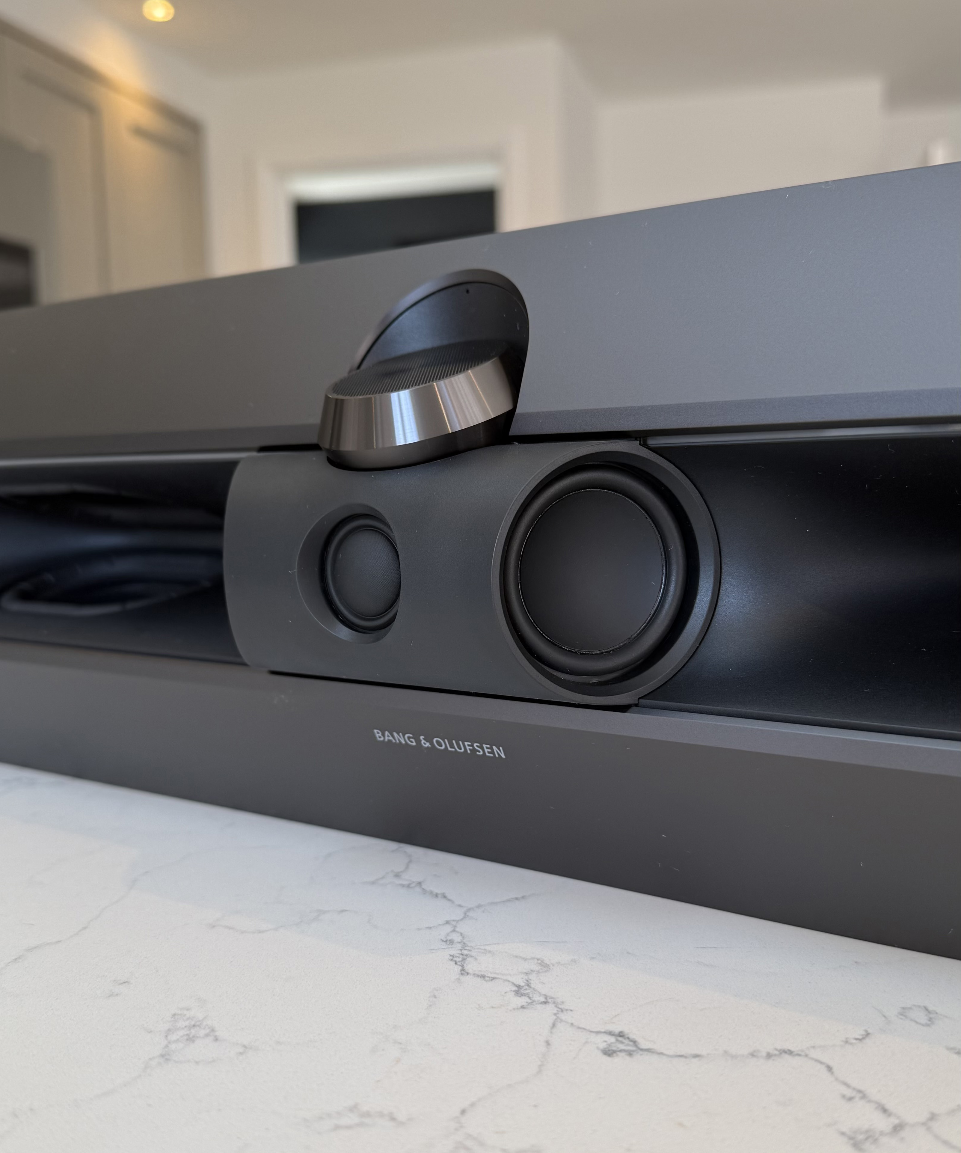 Close-up of the Beosound Premiere front panel showing speaker drivers and central up-firing dial with metallic finish