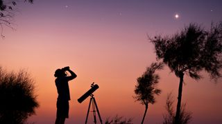 A man looks up at the dawn sky with a pair of binoculars.