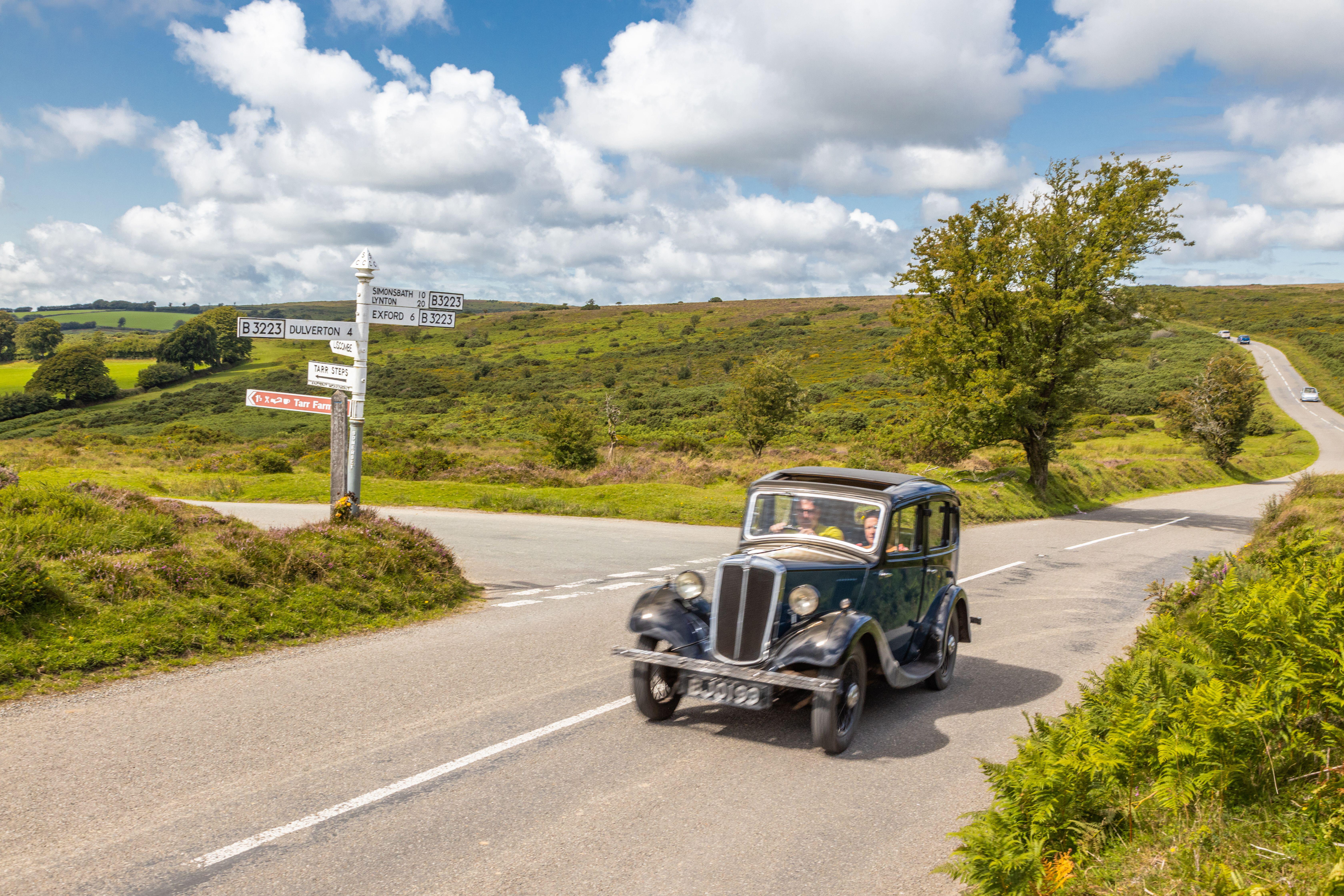  Classic vintage car driving along the B3223 across Exmoor National Park towards Dulverton on a sunny summer day, Devon, England.