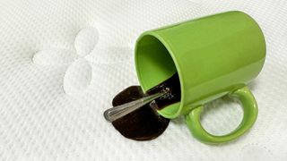 Brown liquid spills out of a green cup onto a white mattress