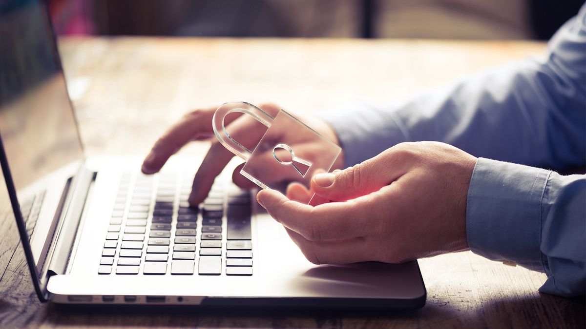 A person typing on a laptop with their right hand while holding a see through padlock in their left