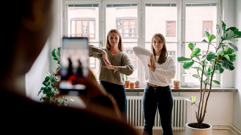 TikTok might have worrying side effect on teenage girls, according to medical report—Teenage girl with mobile phone filming female friends dancing against in living room