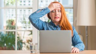 Redhead woman using computer laptop at home stressed with hand on head, shocked with shame and surprise face, angry and frustrated. Fear and upset for mistake.