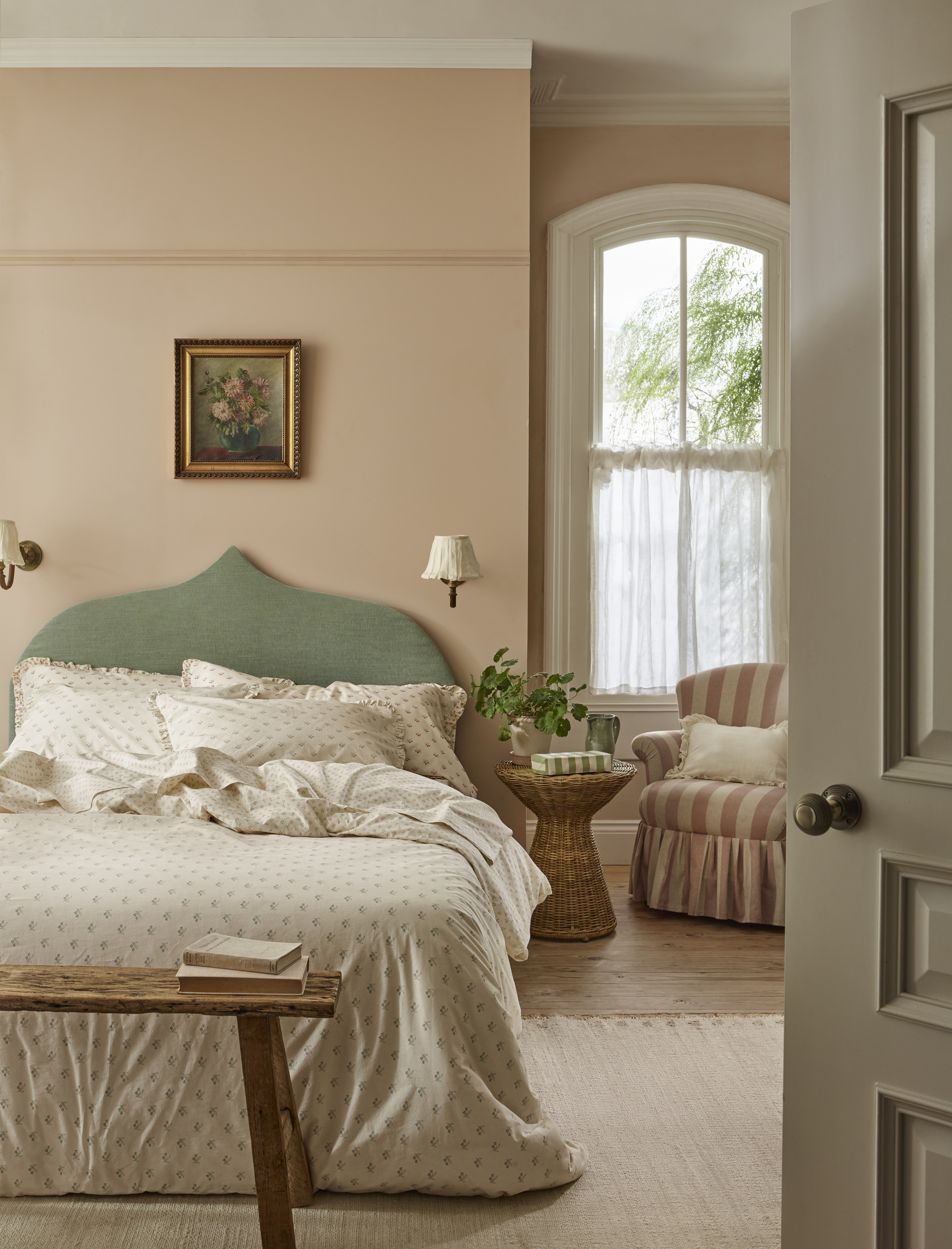 Image of a blush pink, heritage bedroom with a bed that has a green headboard and green and white, dainty floral bedding.