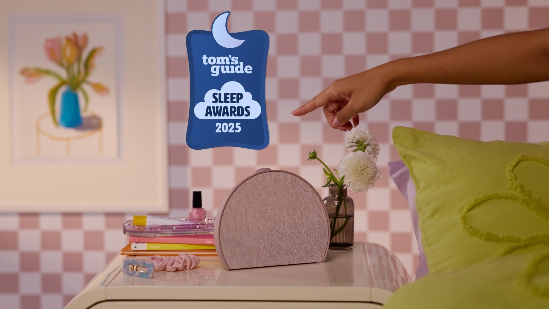 Rosy pink Hatch Restore 3 next to book, hair accessories and plant on bedside table in pink room with check wallpaper and green bedding with Tom&#039;s Guide Sleep Awards 2025 logo