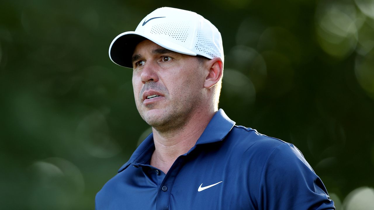 Brooks Koepka from the shoulders up wearing a navy blue polo and white cap