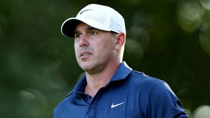 Brooks Koepka from the shoulders up wearing a navy blue polo and white cap