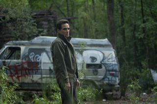 Yul Vazquez, who plays Yunis Sablo, stands in a forest near a van covered in graffiti in season 1 episode 10 of The Outsider