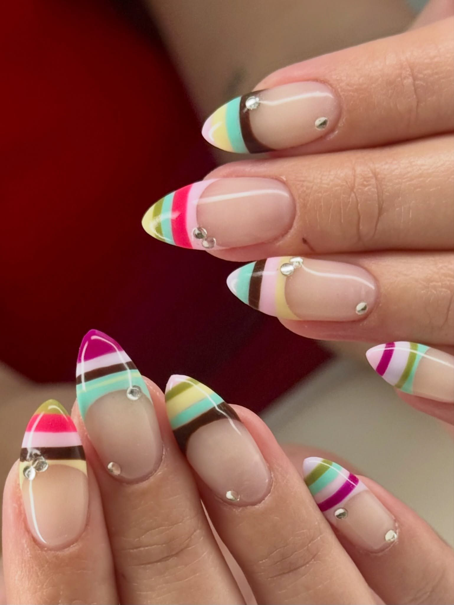 almond nails with colorful striped French tips in pink, mint, yellow, brown, and white with small crystals