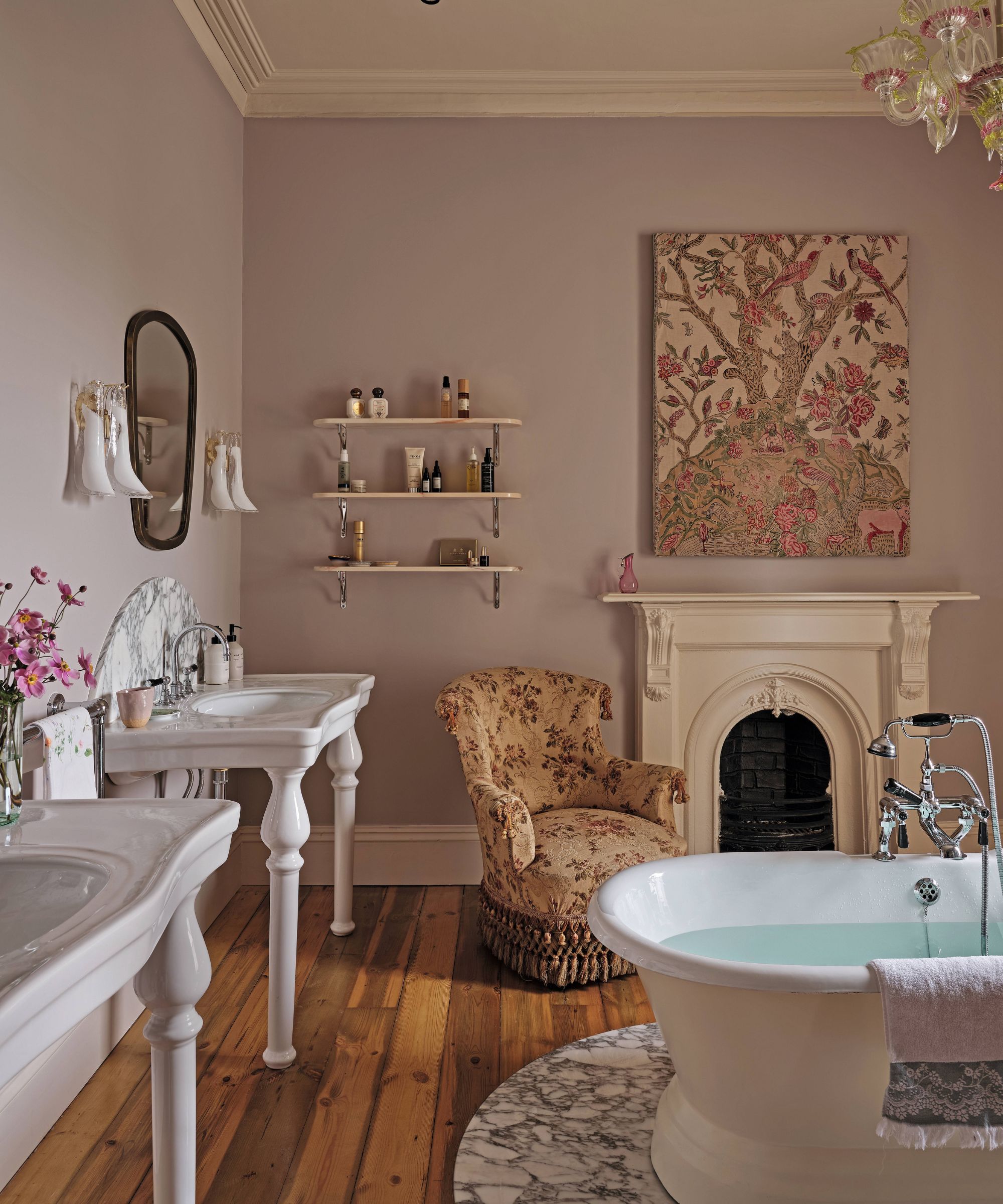 a lilac painted bathroom with traditional Victiorian bath tub and vanity sinks, fireplace and floral art and small chair