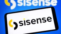 The Sisense logo on a phone, held in front of a blurred Sisense logo shown on a larger screen.