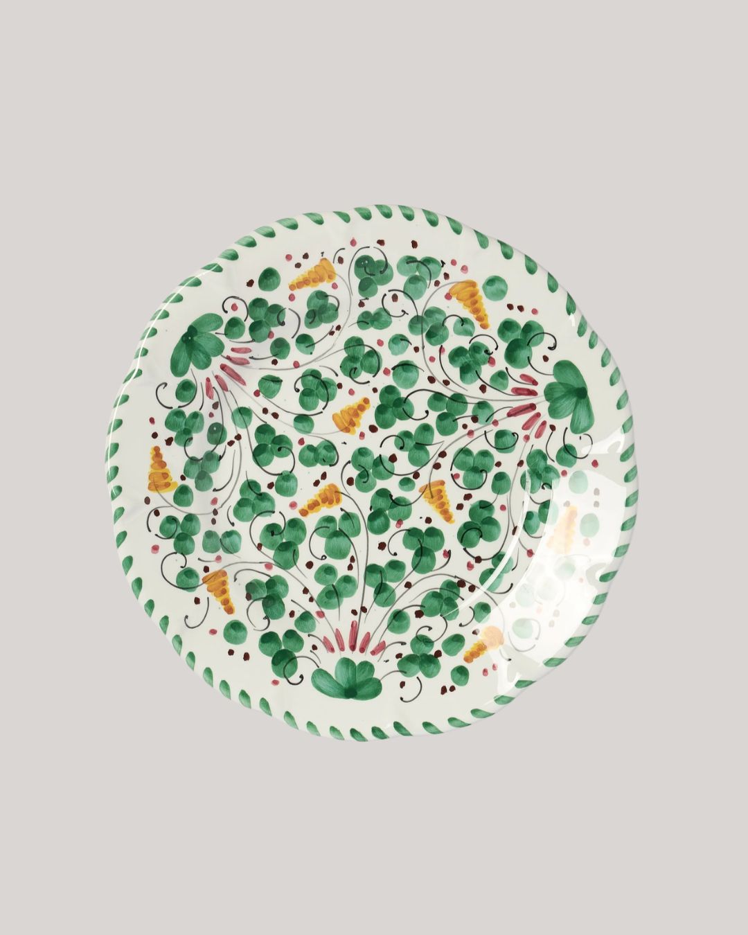 A patterned ceramic plate with a white background and a leafy, green, yellow, and red motif, shown against a gray background.