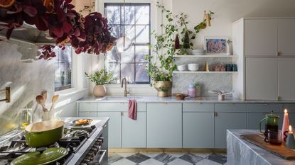 a pale blue modern kitchen in a historic home with checkerboard floor decorated for christmas with a red foliage and orange garland over the stove and little bottle brush trees and candles