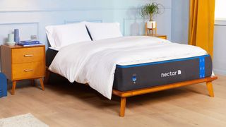 Nectar Memory Foam Mattress shown on a light wooden bed frame and dressed with white pillows and sheets
