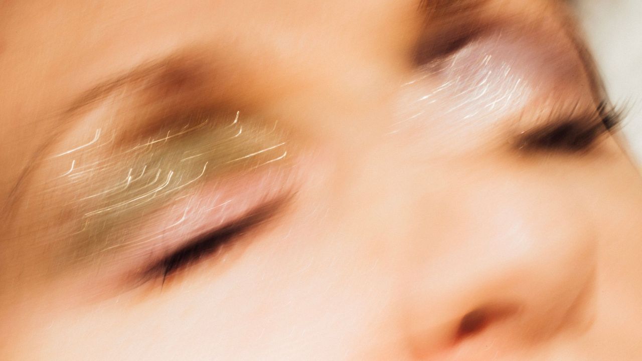 Closeup of a woman wearing glitter eyeshadow and tubing mascara. Young woman has her eyes closed and long eyelashes. 