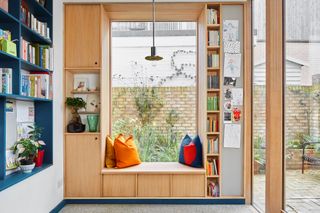 Built-in wooden window seat with cushions, surrounded by shelving for cookbooks