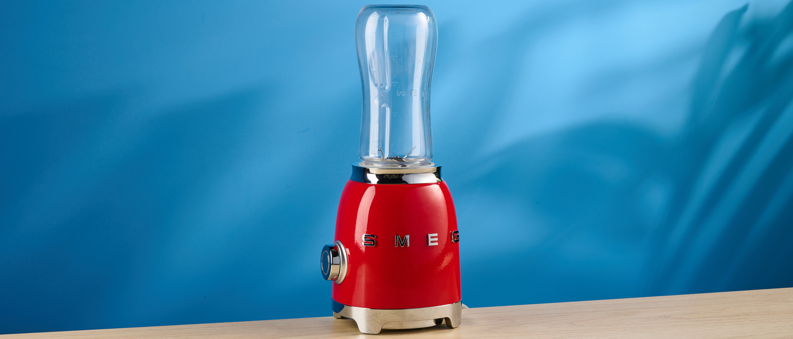 Smeg Personal Blender in the red colorways photographed in front of a blue background.