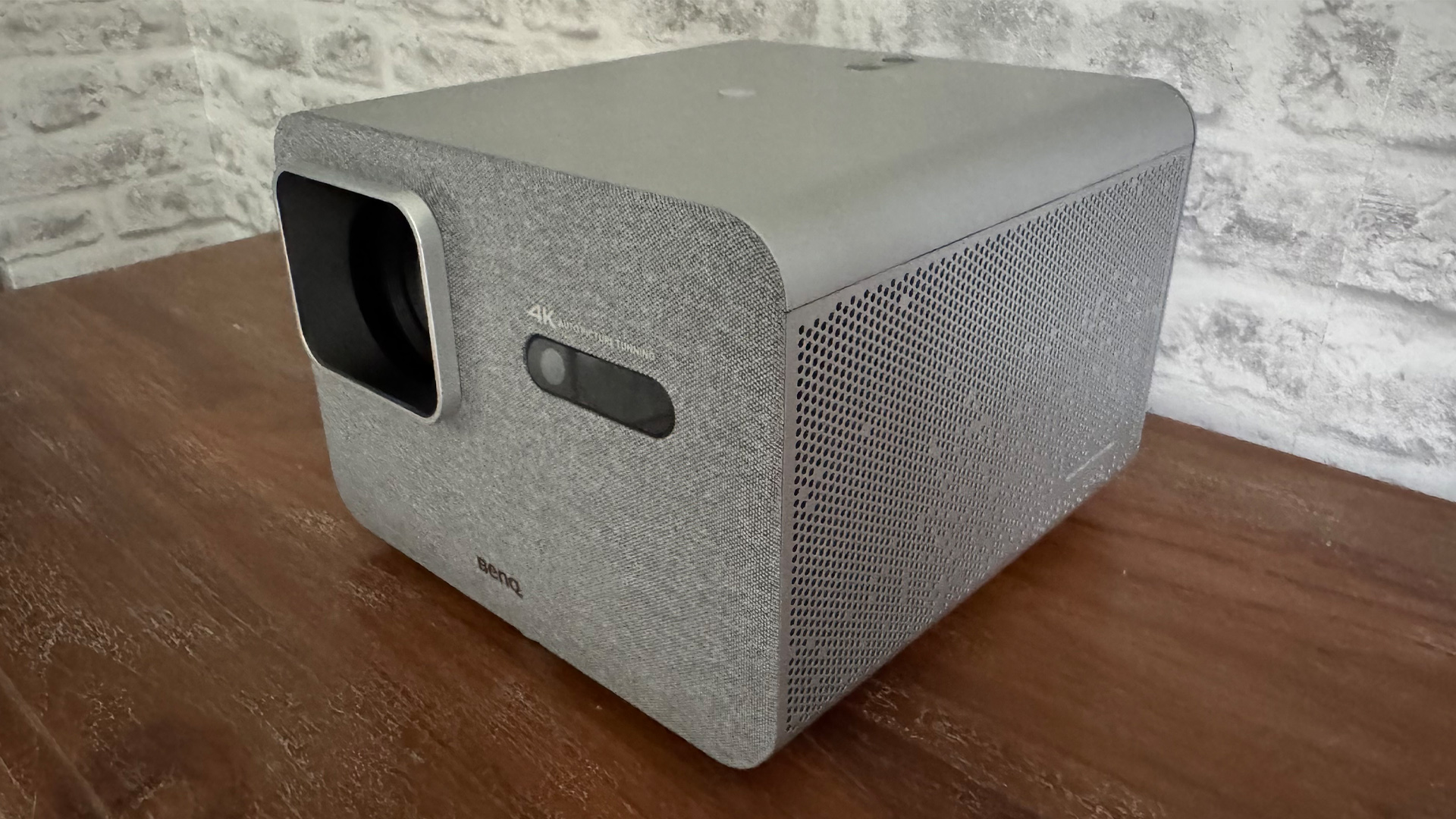 BenQ TK705i home cinema projector on wooden sideboard in front of white brick wall