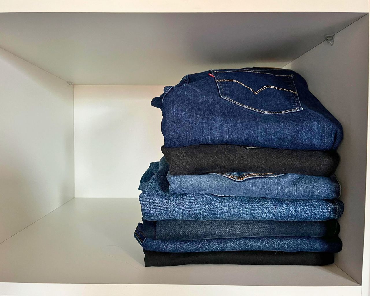 Seven pairs of neatly stacked black or blue jeans