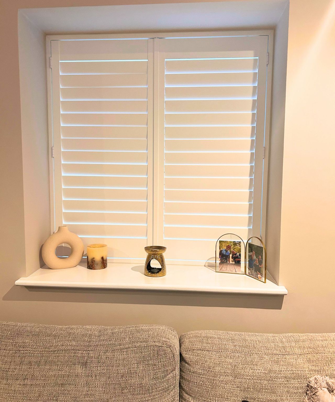 A neat living room with white shutters, candles, oil burner and gold frame