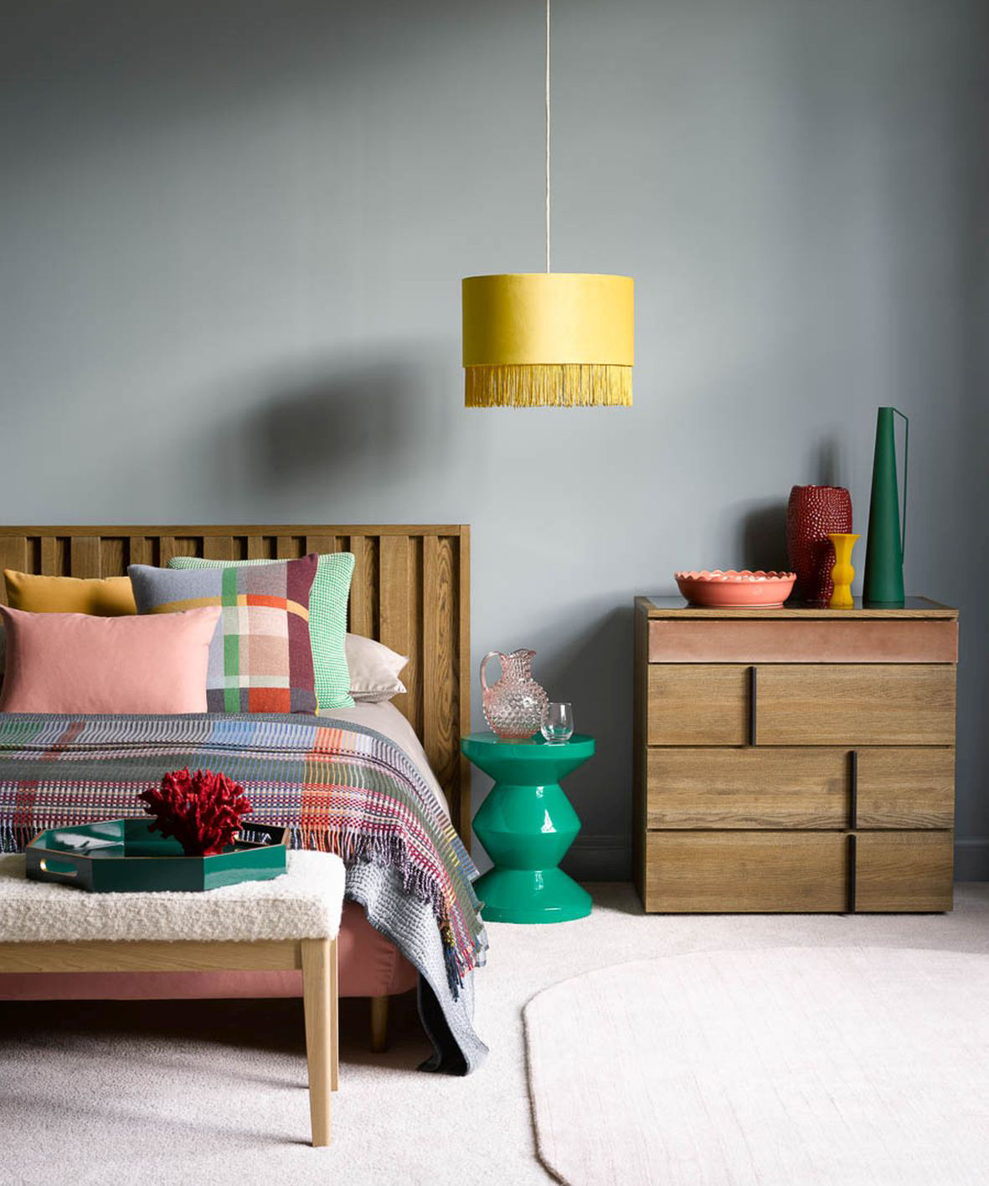 Bright and cheerful check and color block bedding, fringed yellow drum shade, and modernist wooden furniture in cozy bedroom scheme.