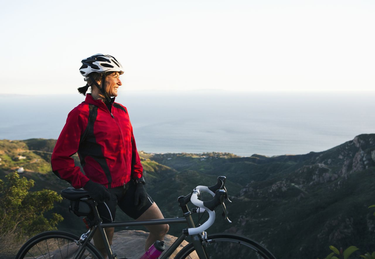 A mature woman pauses to look at the view as she cycles up a mountain. 