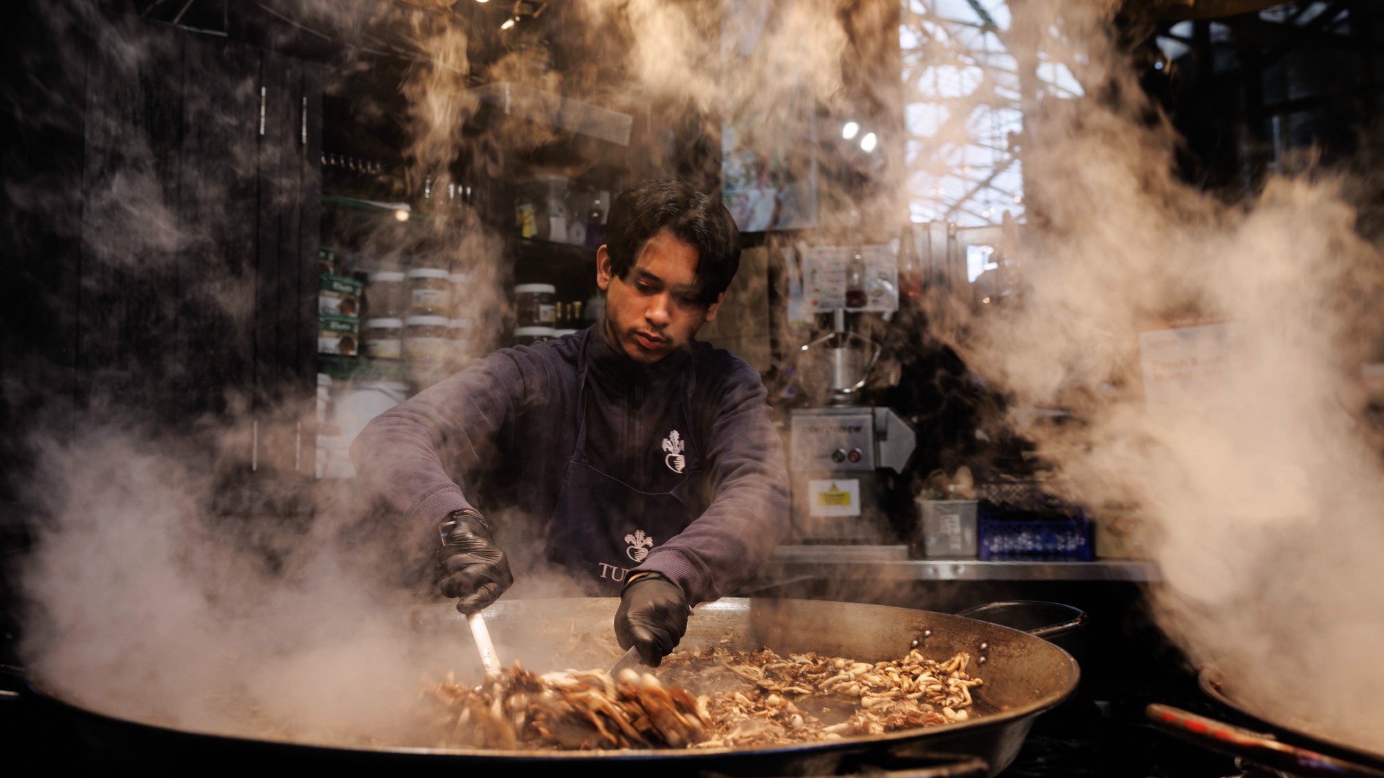 A man cooks mushrooms in a giant pan at Borough Market