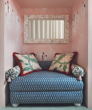 loveseat that fills entire crevice in room with blue pattern and walls painted pink and shell mirror behind