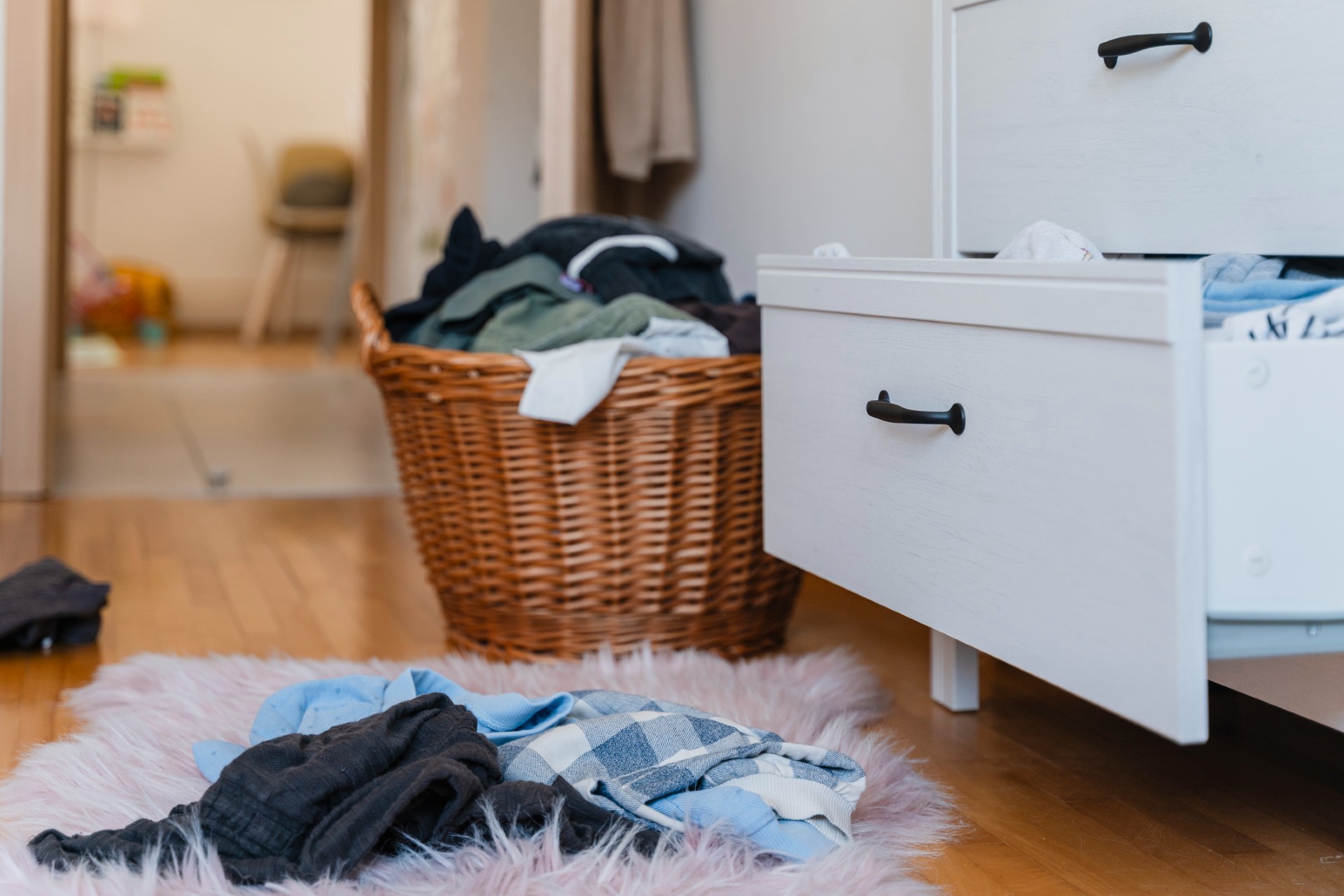 clothes pile in a wicker laundry basket and clothes on the floor in a rug and an open drawer