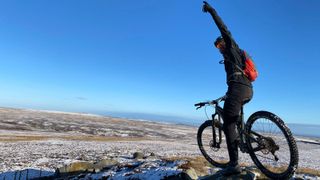 A mountain biker with a raised hand on top of a snowy ridge