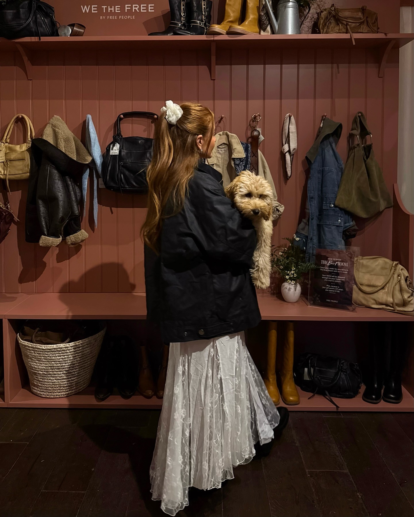 A woman in a barn jacket holding a puppy with a half-up, half-down ponytail hairstyle