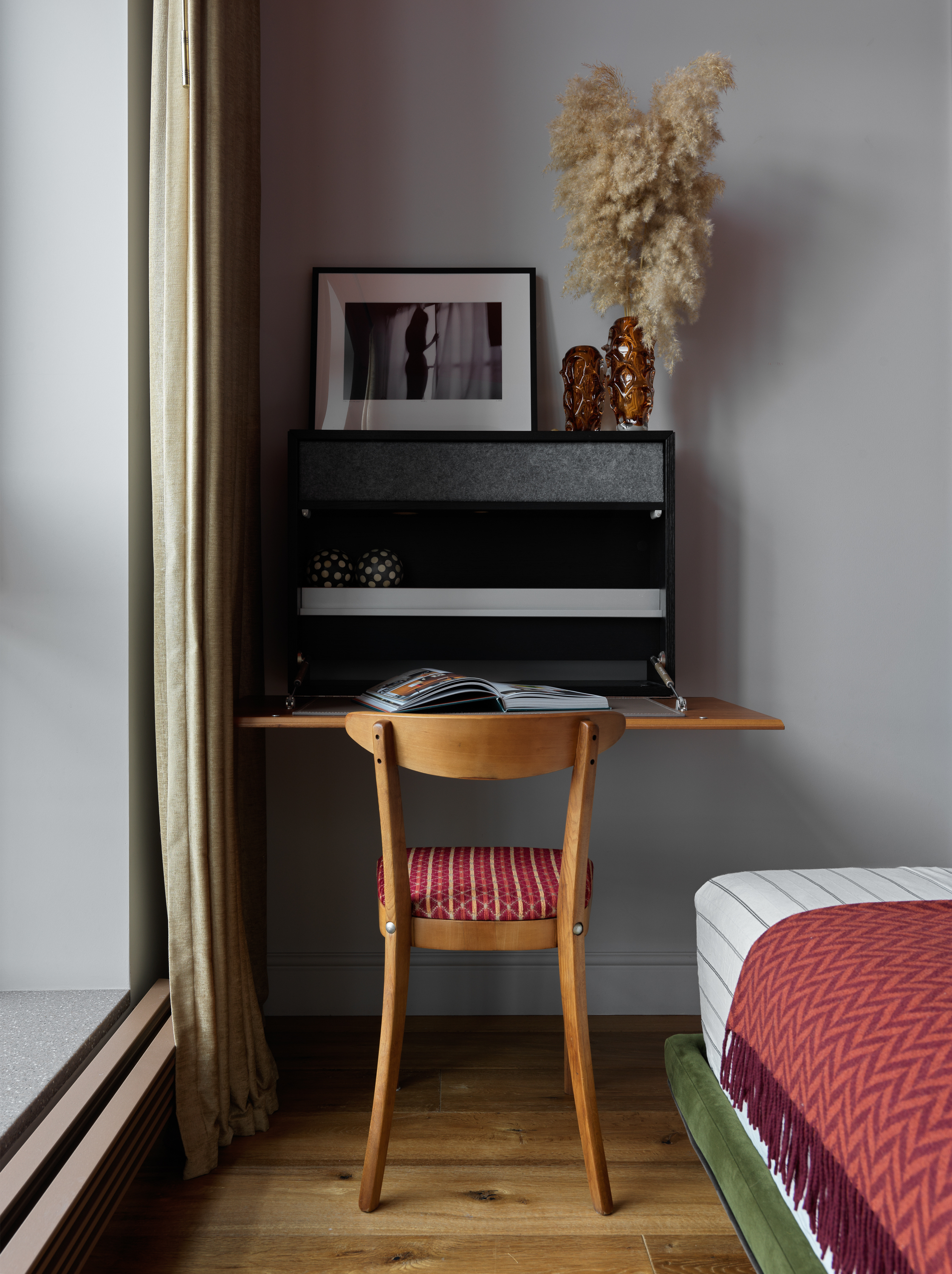 A bedroom with a fold out desk decorated with a black and white picture and two vases, one filled with pampas grass