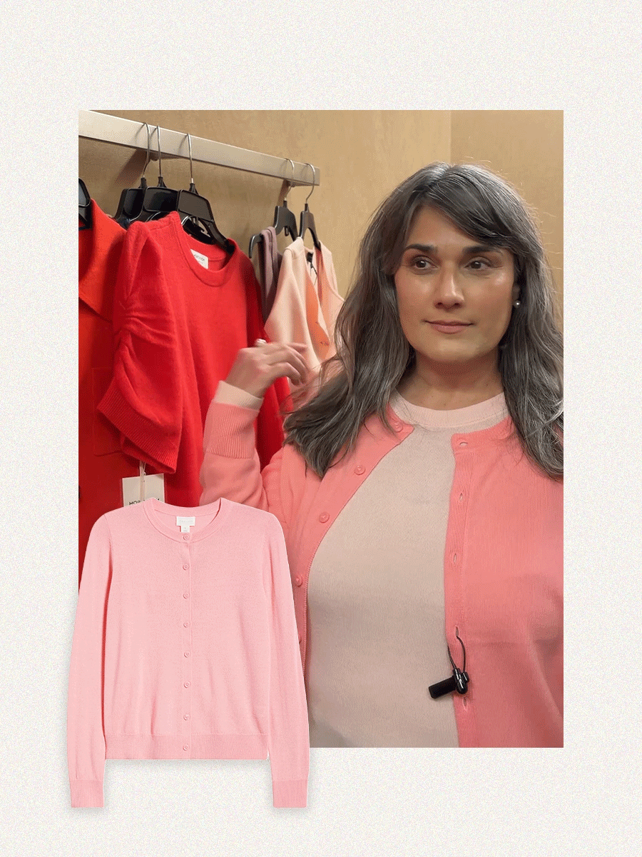 A woman with gray hair trying on a coral cardigan and blush pink top.