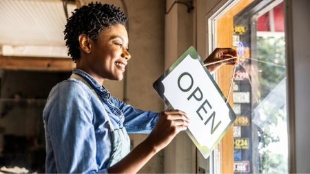 Female small business owner placing open sign in shop window 