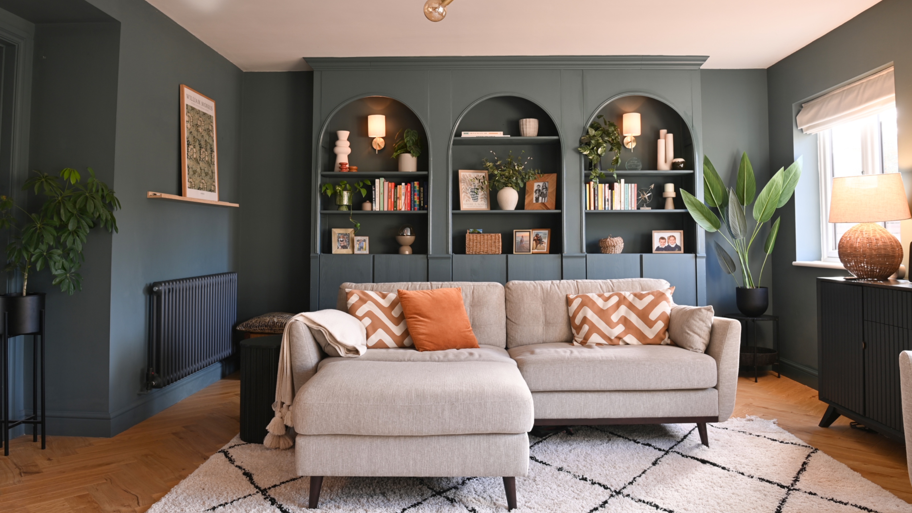 dark blue living room with beige L shaped sofa, rug, wooden floor, bespoke shelving 