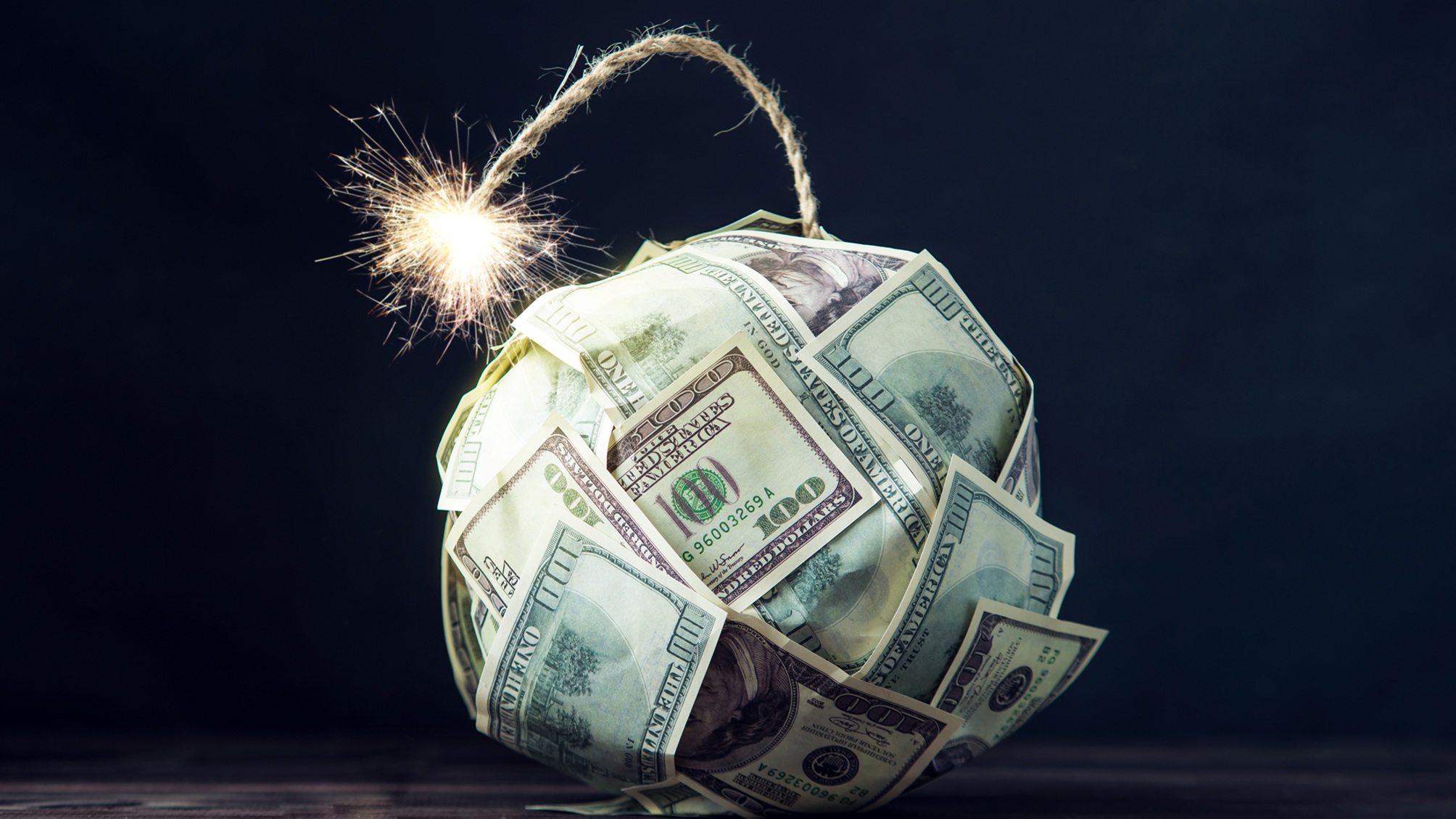 A ball made of hundred-dollar bills has a lit fuse.