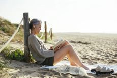 Woman sitting on the beach reading a book.