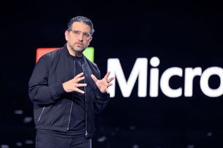 Panos Panay on stage with a Microsoft logo behind him.