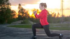 white woman red top black leggings doing split squat in park at sunset